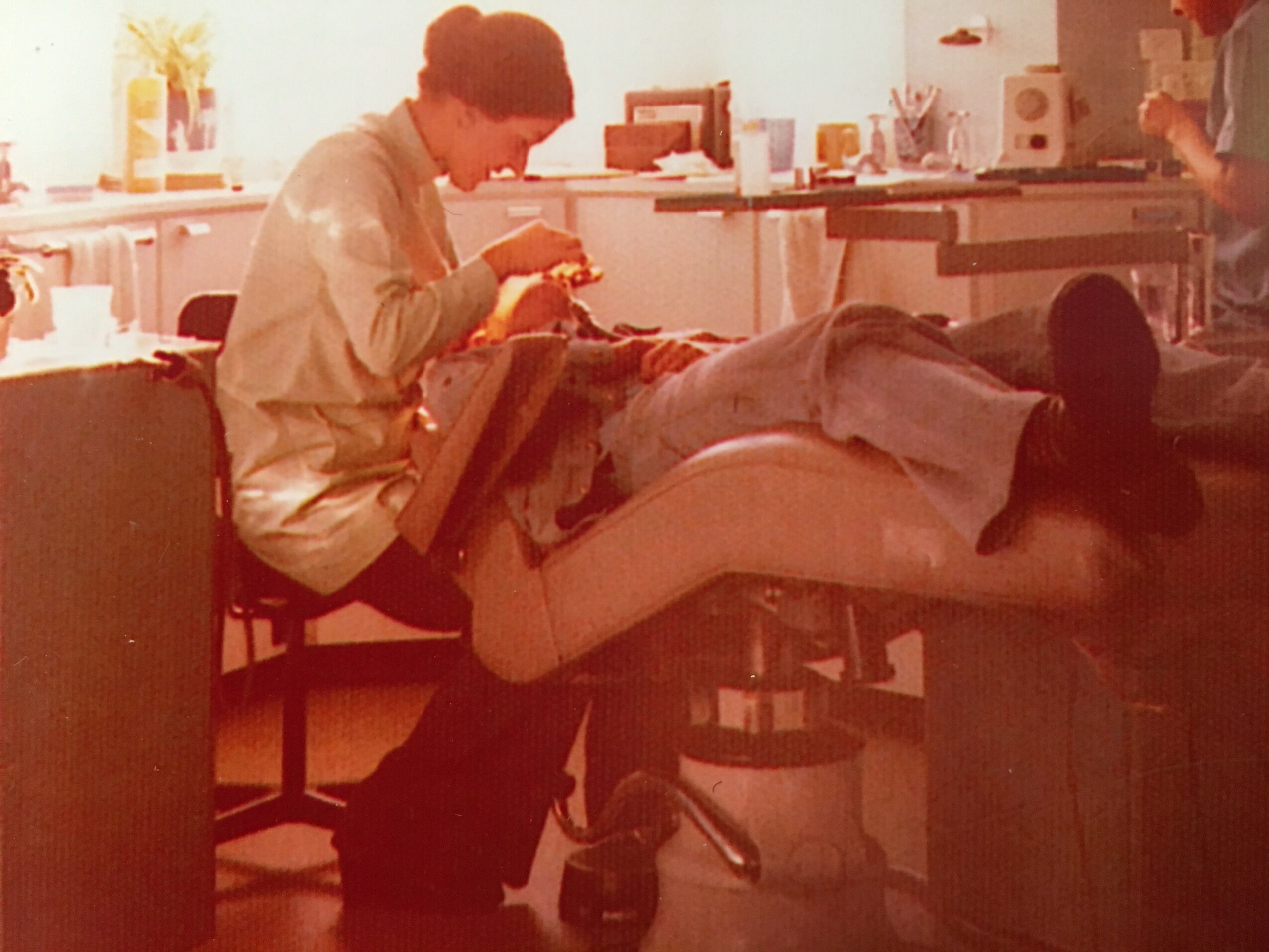 Person sitting on a chair, leaning over a table, working on a project in a room with bright sunlight.