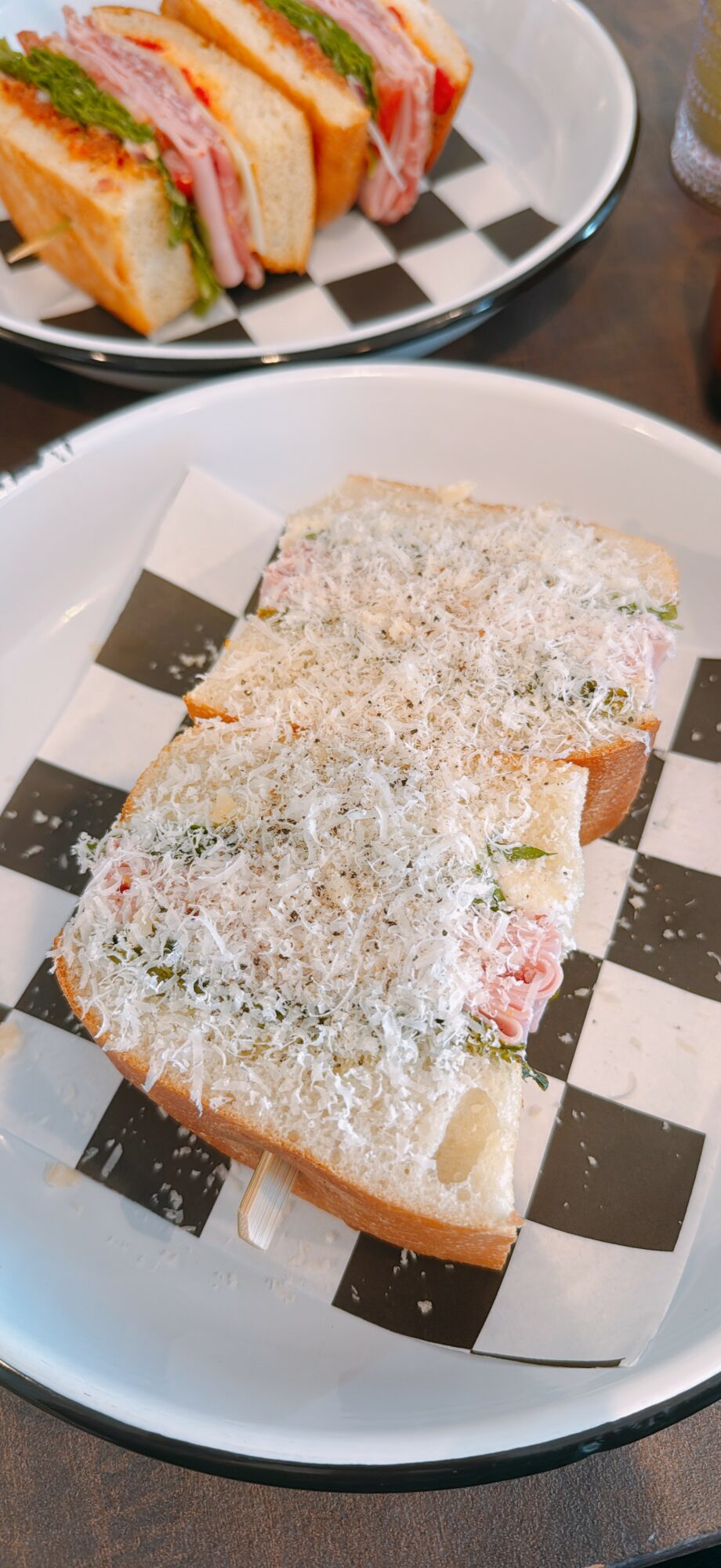 Slice of bread topped with cheese and herbs on checkered paper, on a white plate.
