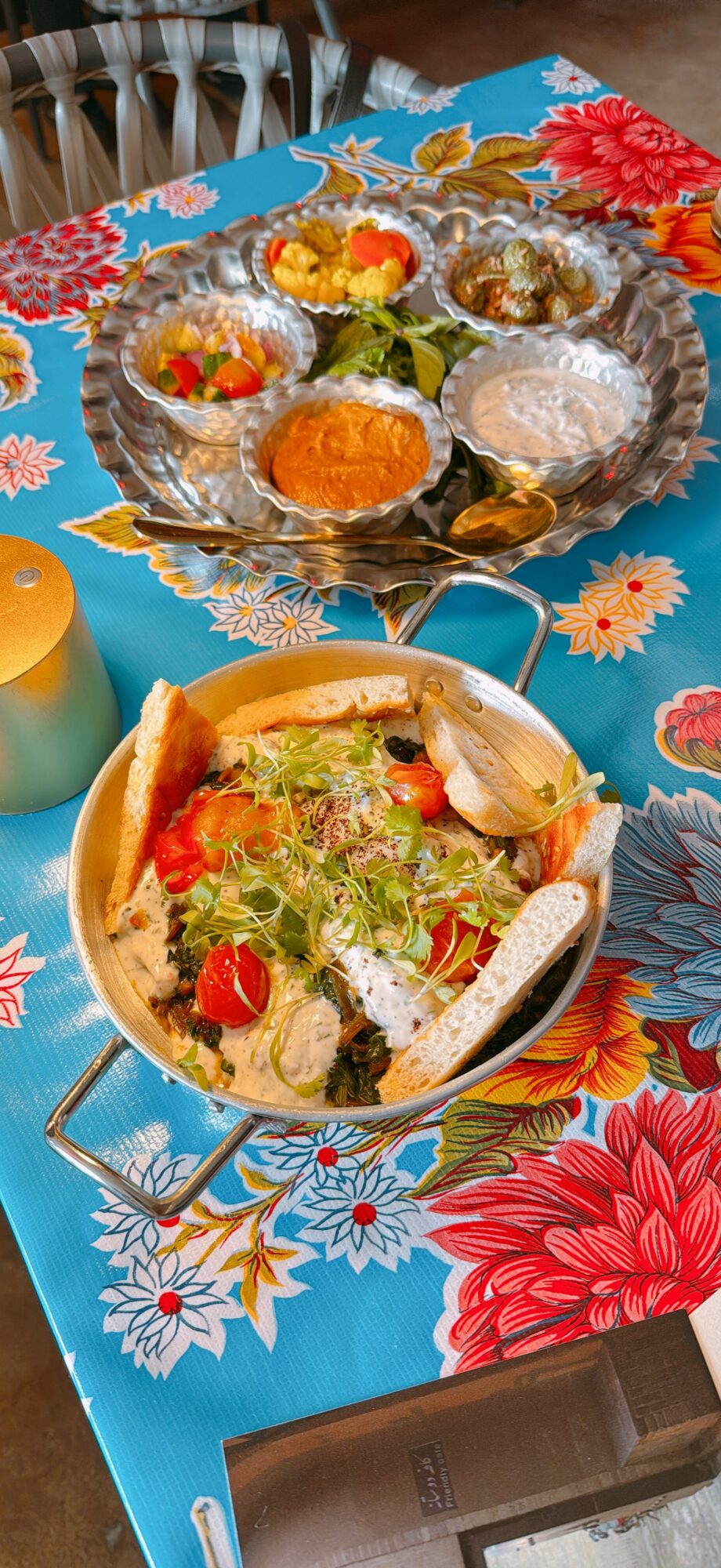 Colorful table with a bowl of salad and a tray of assorted sweets on a floral tablecloth.