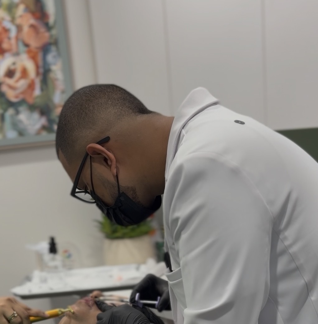 Person wearing glasses and a face mask, leaning over a table in a room with a floral painting and white wall.