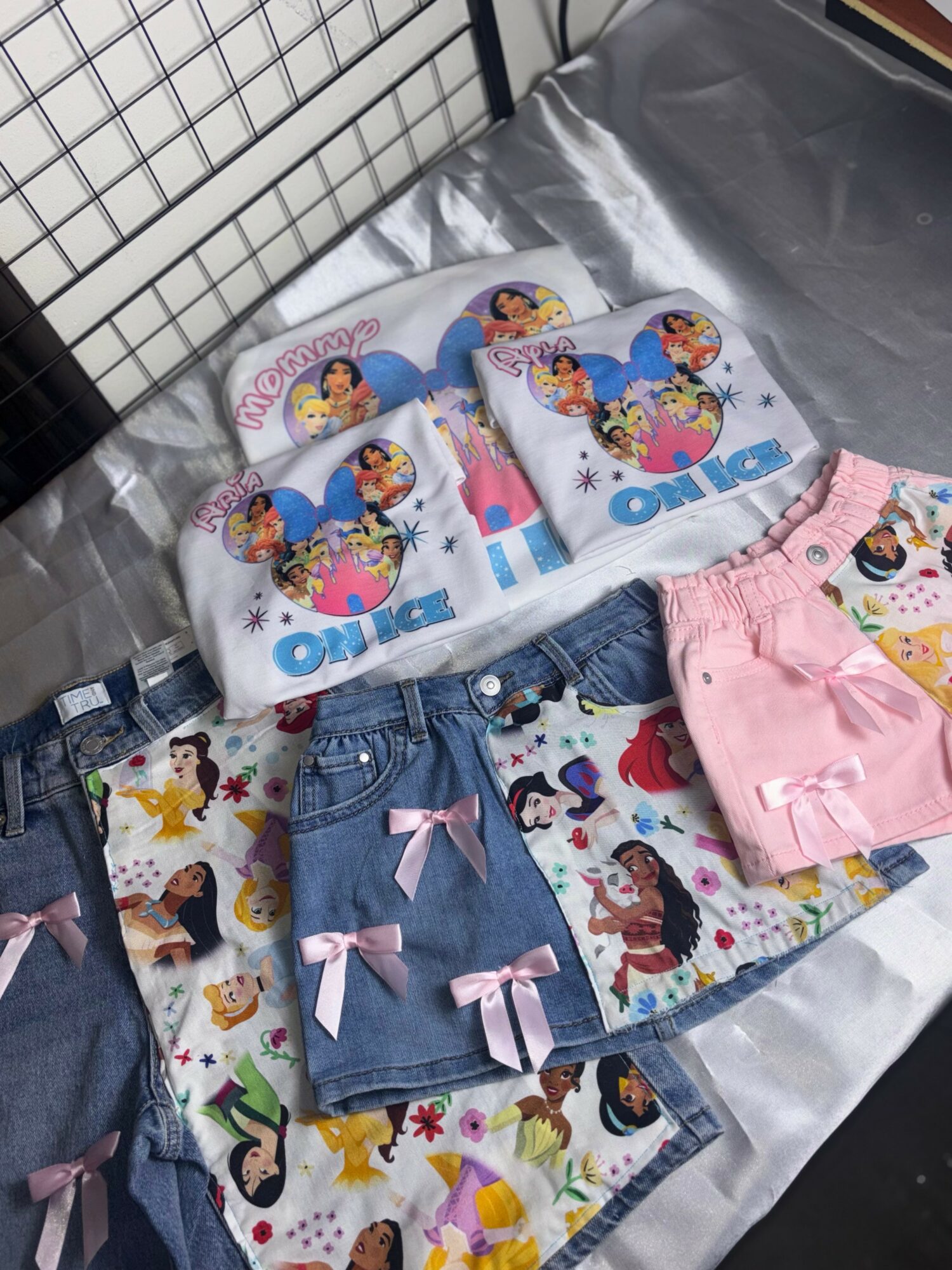 Children's clothing and accessories with Disney princess and unicorn designs, including socks, shorts, and a towel, displayed on a table.