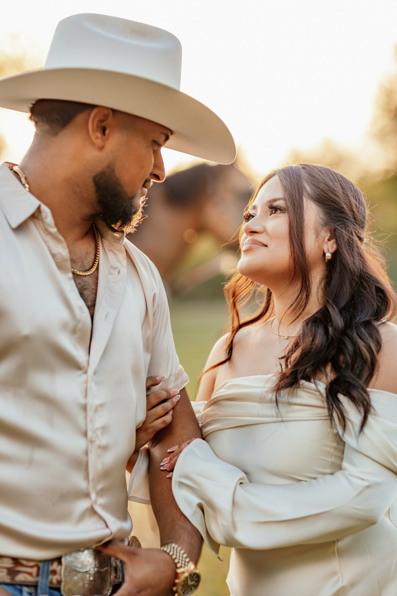 A man and woman face each other outdoors, holding hands, with warm sunlight in the background.