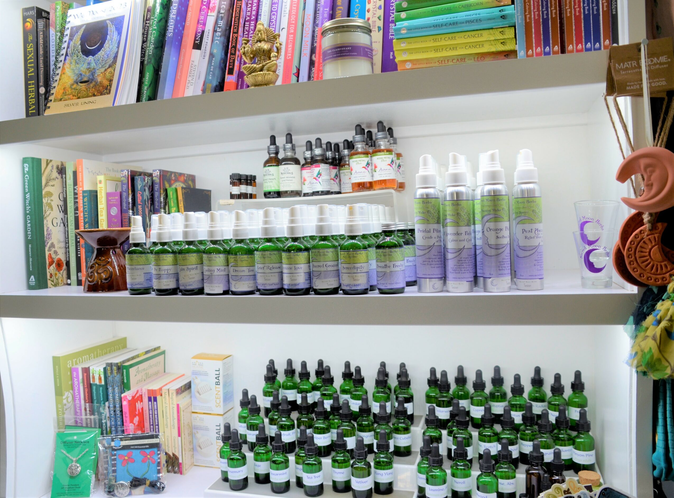 Shelves with colorful books and essential oils bottles, some with droppers, arranged on white shelves.