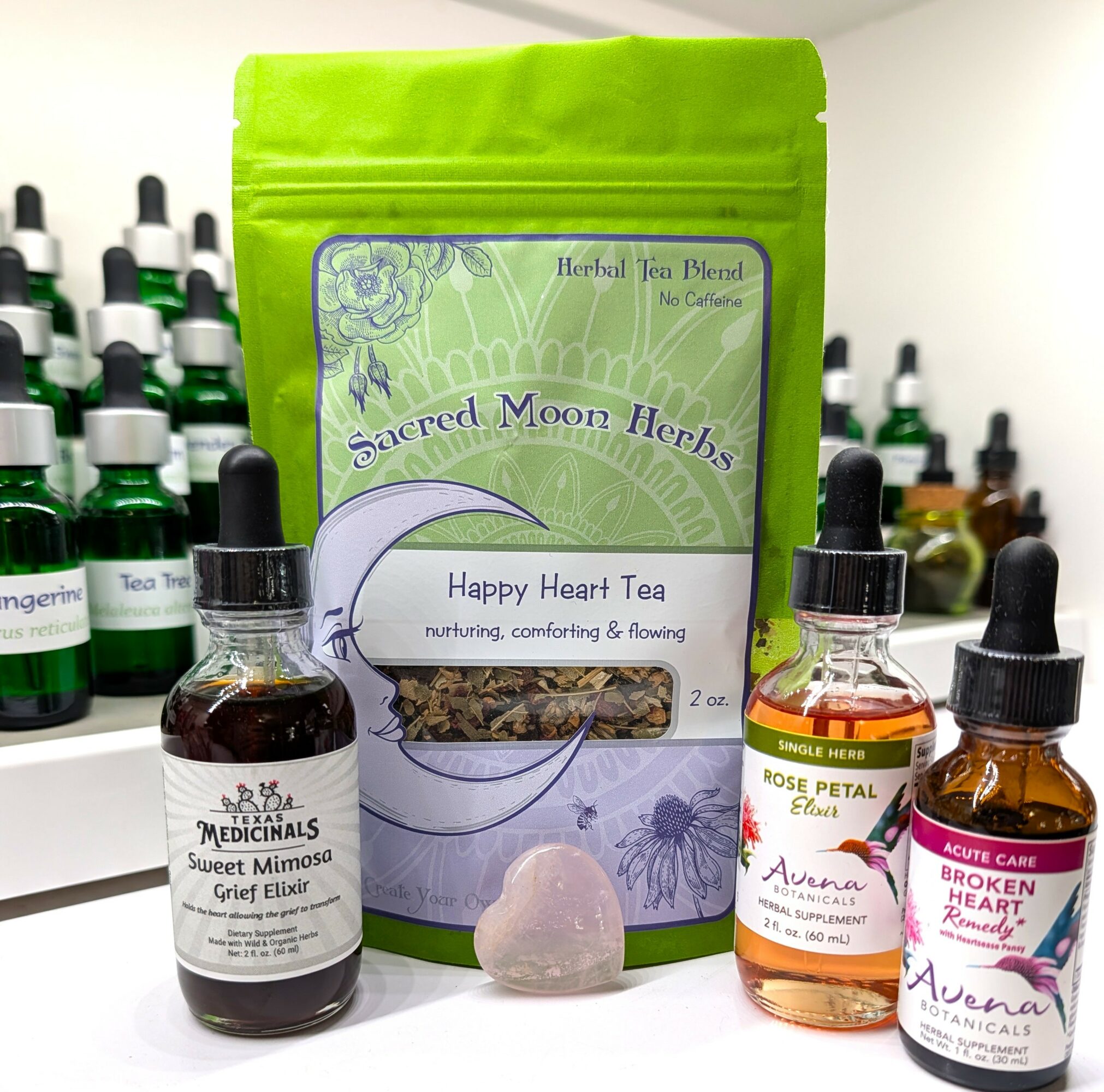 Three small bottles and a green herbal tea package on a white surface, with bottles of herbal remedies in the background.