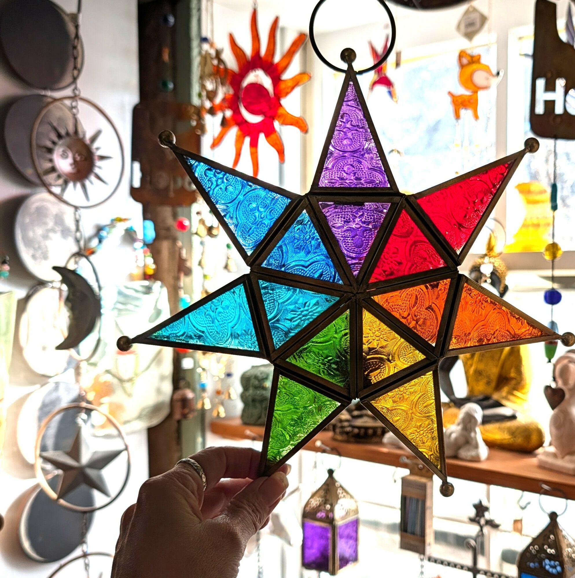 Hand holding a colorful star-shaped lantern with various decorations in the background.