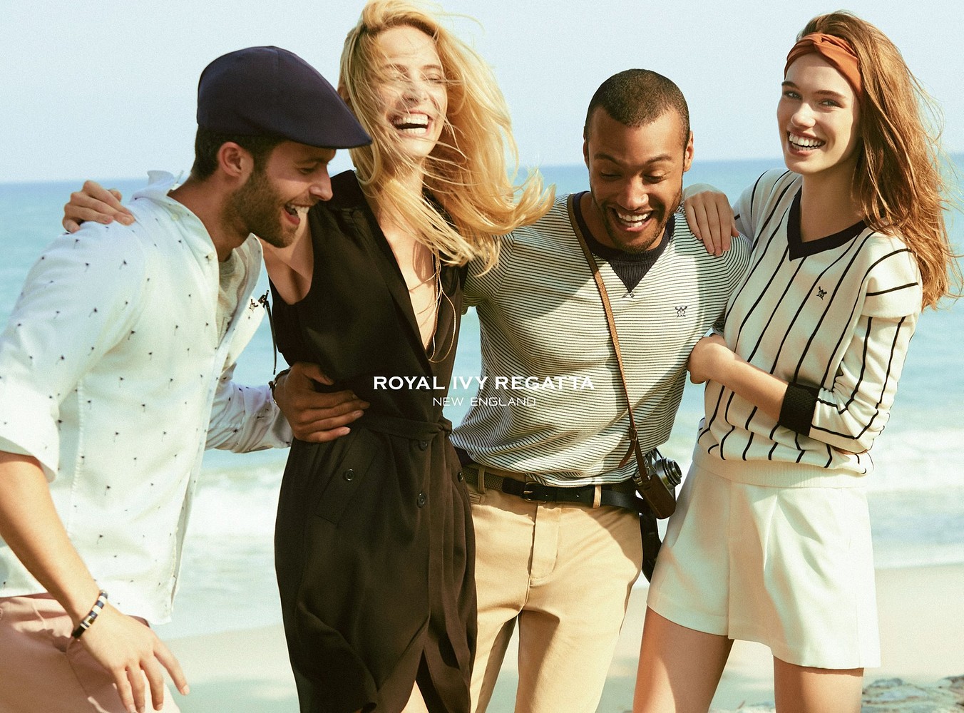 Four people smiling and laughing together outdoors, with a beach and ocean in the background.