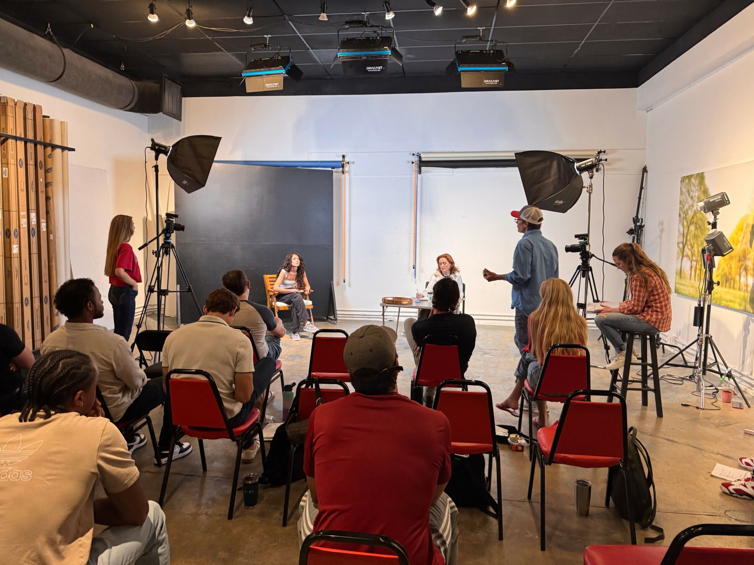 People seated at tables in a room with a blackboard and speakers, viewed from the front, upside down.