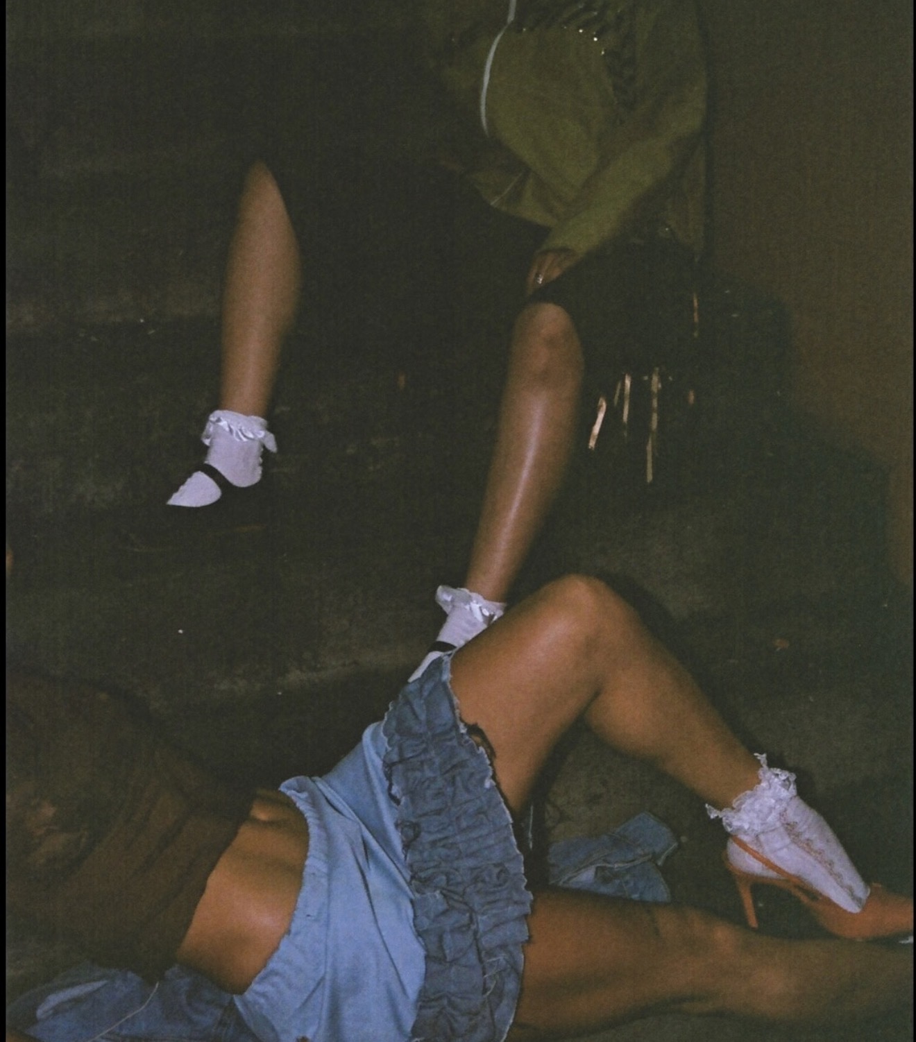 Person lying on the floor with legs extended, wearing denim shorts and white shoes, with another person sitting nearby.