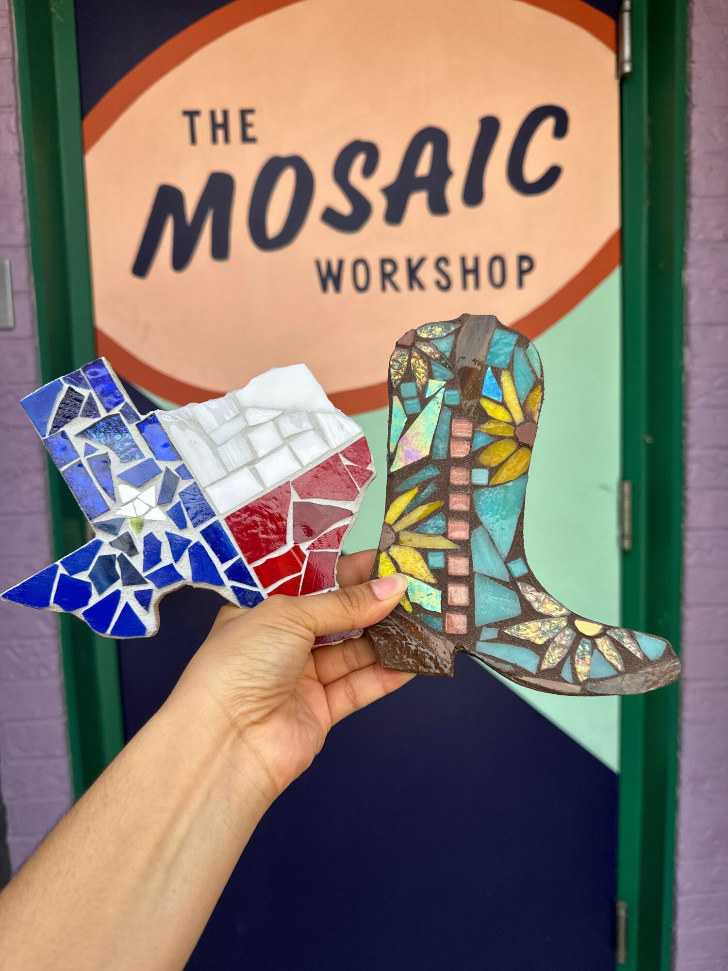 Hand holding a mosaic sculpture of a dog, with a workshop sign in the background.
