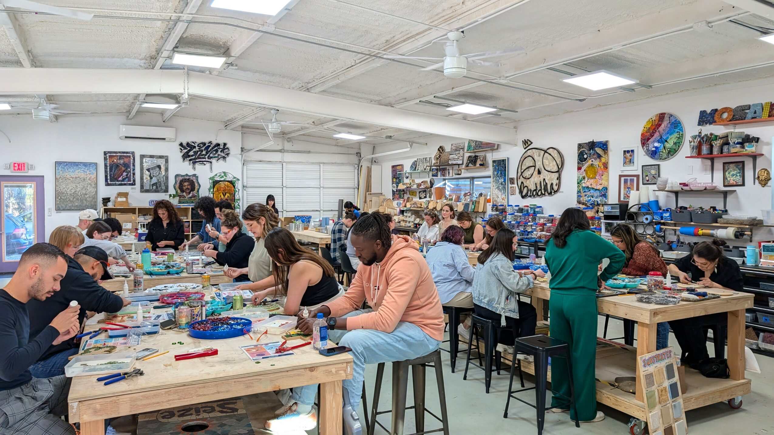 People working at tables in a large, well-lit art studio with various artworks on the walls.