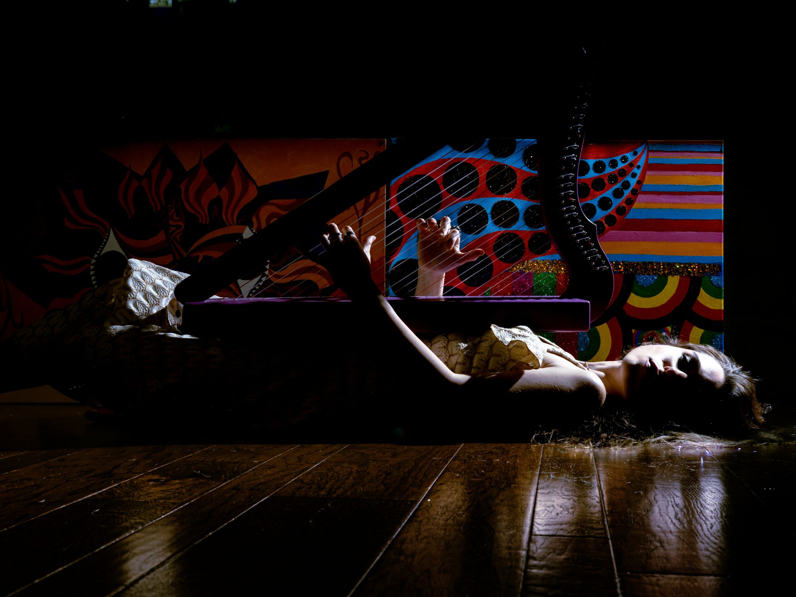 Person lying on the floor with colorful, patterned artwork in the background, dim lighting, wooden floor, and relaxed pose.