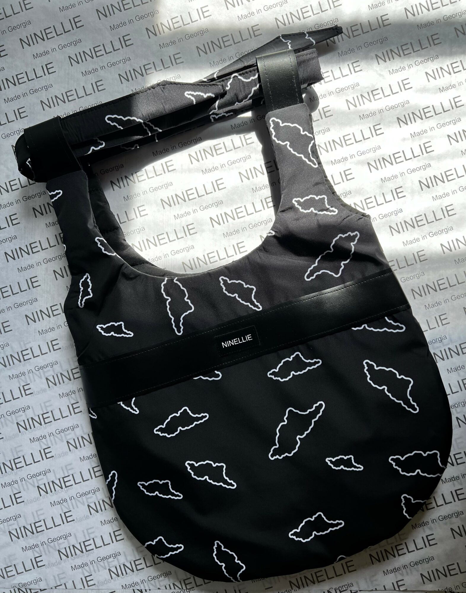 Black bag with white cloud pattern, hanging on a display, background with repeated text 'NINELLE'.