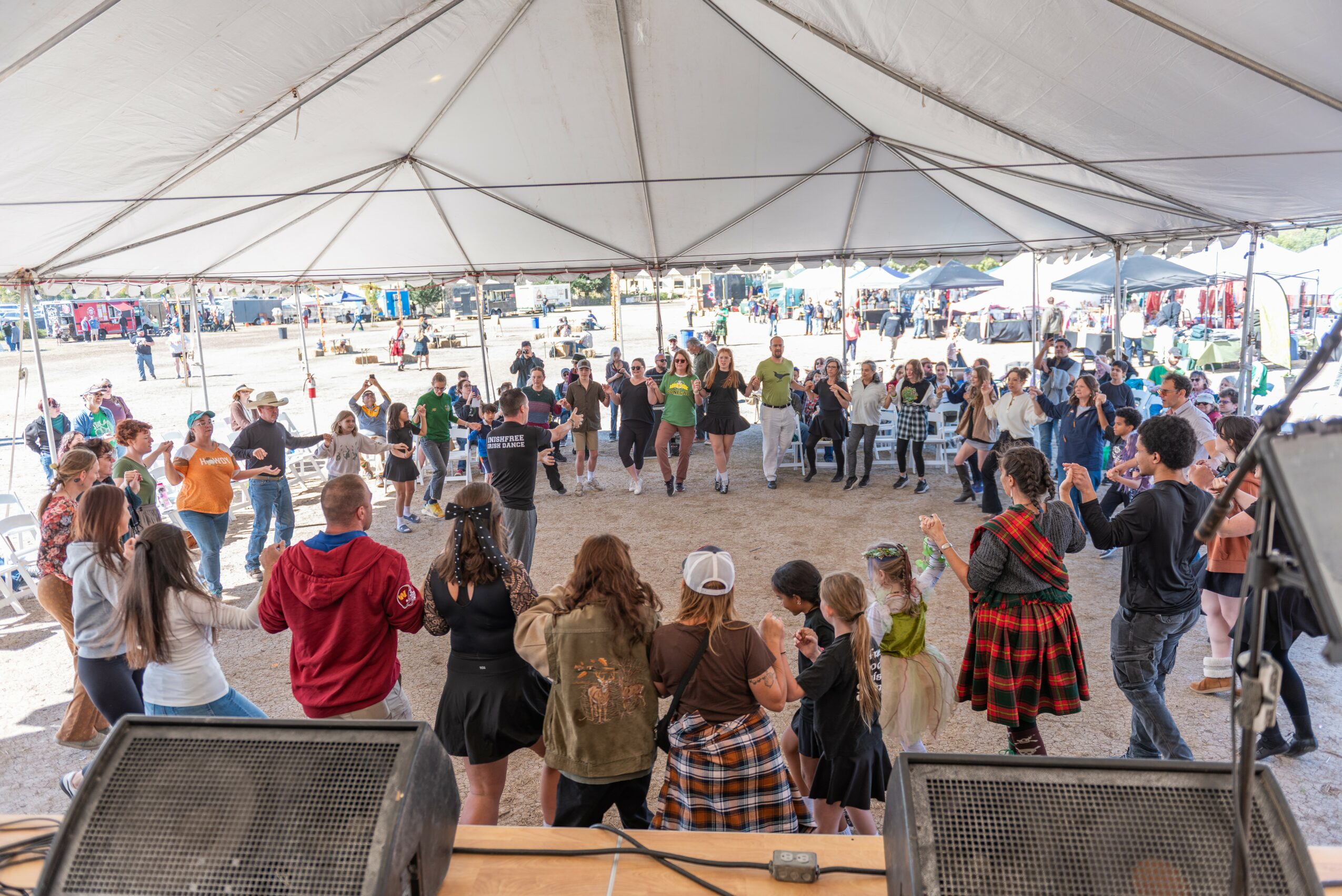 People dancing and socializing under a large tent at an outdoor event, with a crowd in the background.