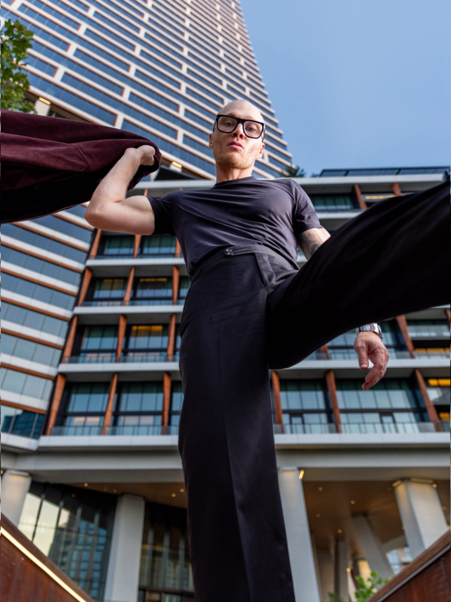 Low-angle view of a woman in black clothing and sunglasses standing in front of a tall building.
