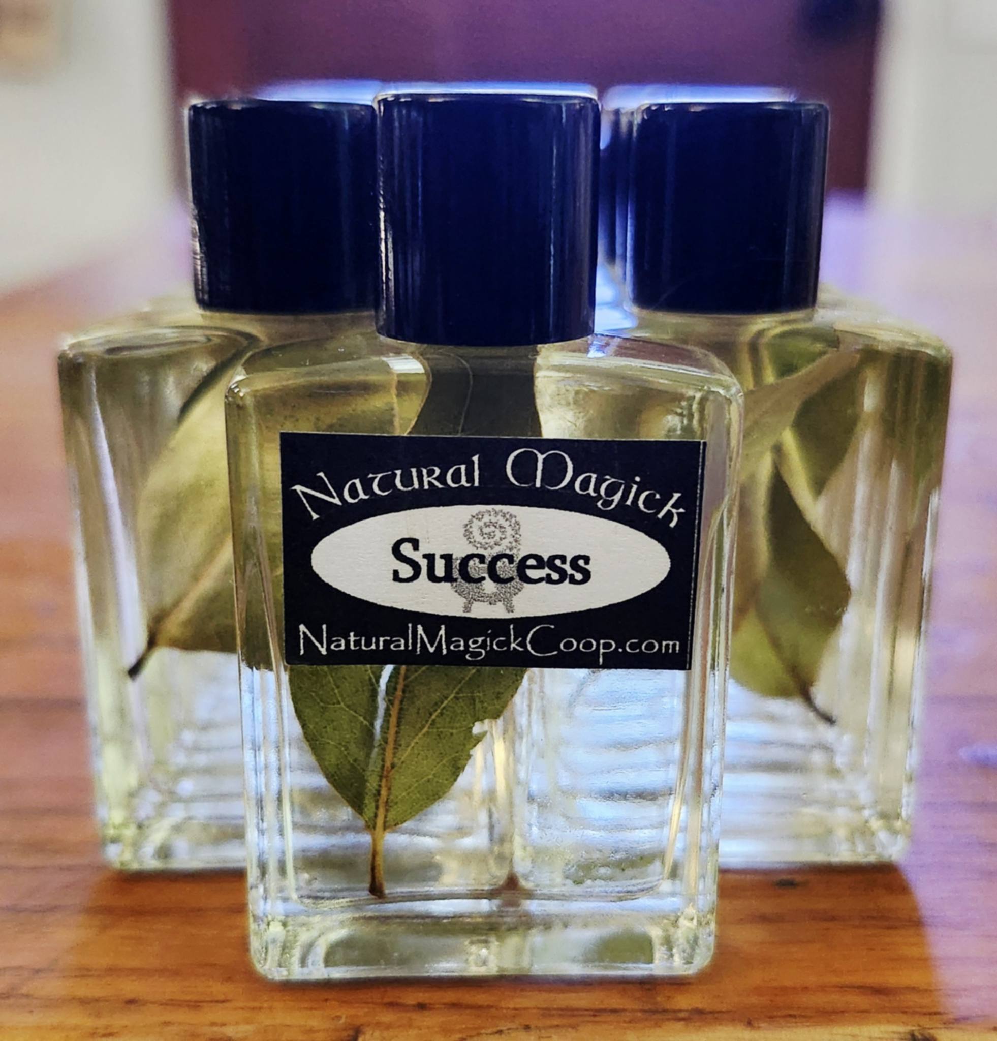 Three small glass bottles with blue caps and a label reading 'Success' and 'Natural Magick' on a wooden surface.