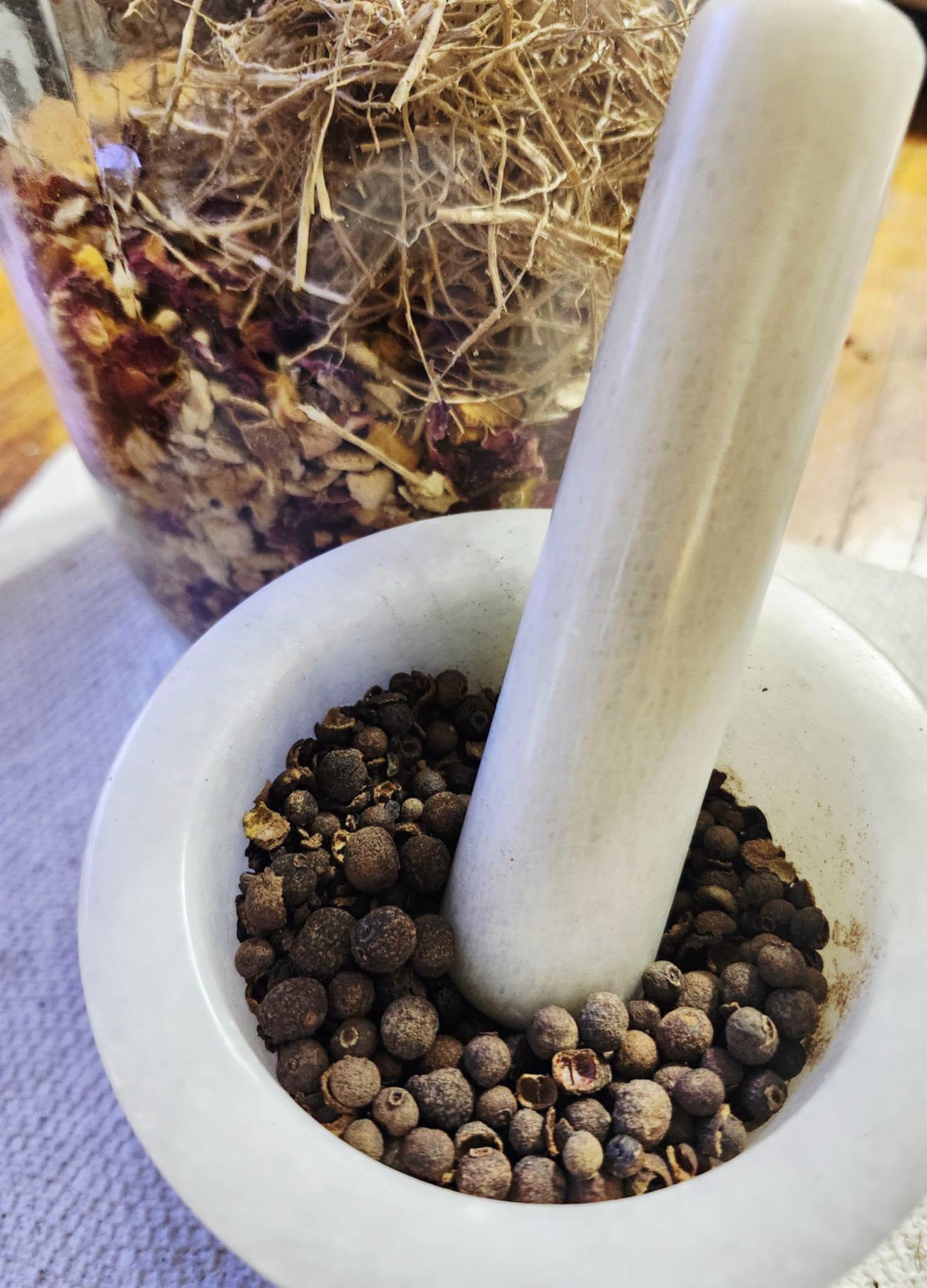 White mortar and pestle filled with black peppercorns, with a plant in the background.