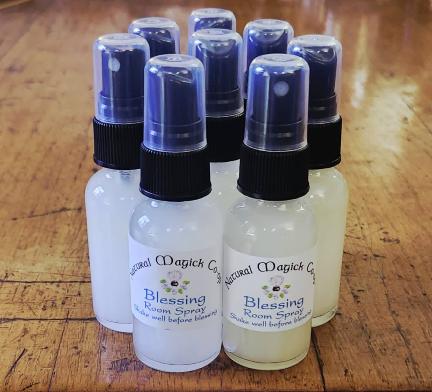 Seven small spray bottles with blue caps and labels on a wooden surface.