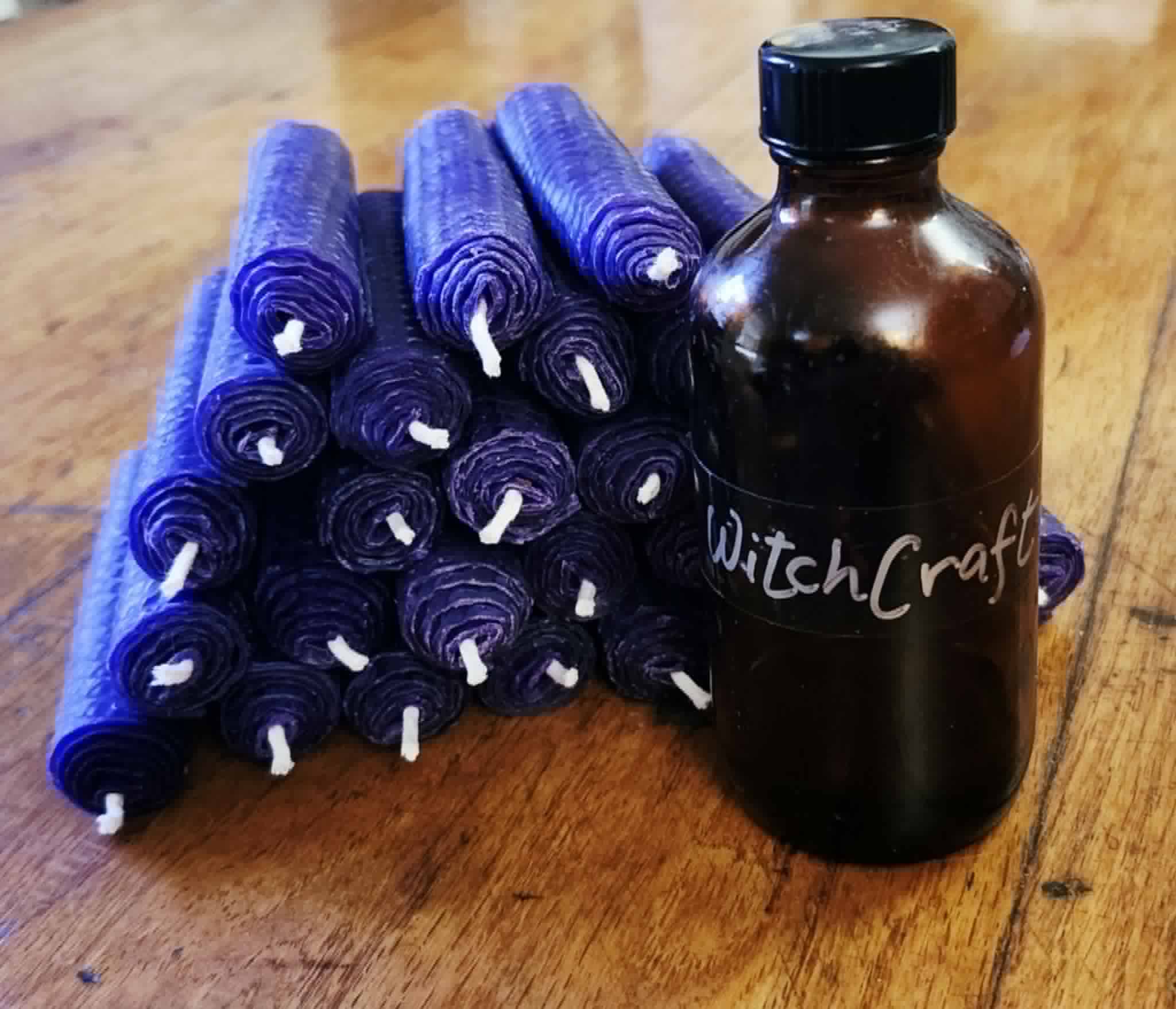 Group of purple rolled candles and a dark brown bottle labeled 'WitchCraft' on wooden surface.