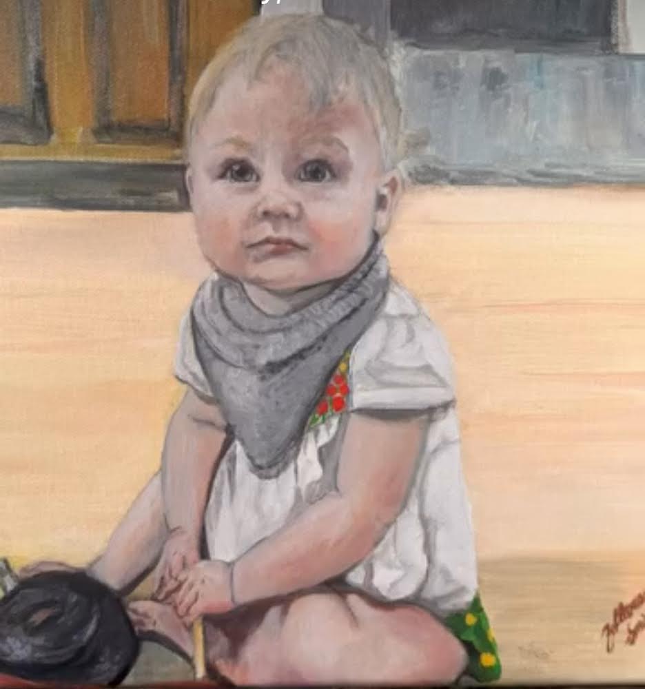 Child sitting on the floor with a gray bandana, wearing a white shirt, looking at the camera.
