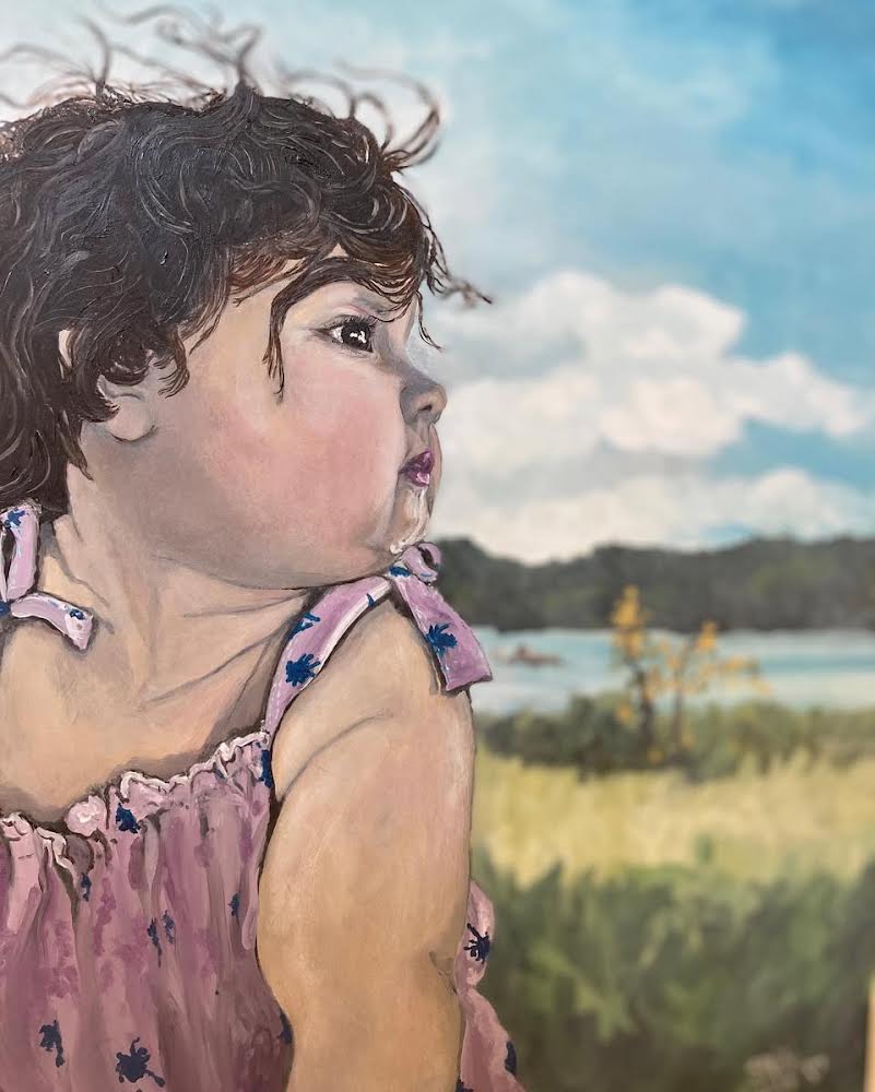 Child with curly hair looking to the right outdoors, sky and landscape in background, wearing a pink dress with ruffles.