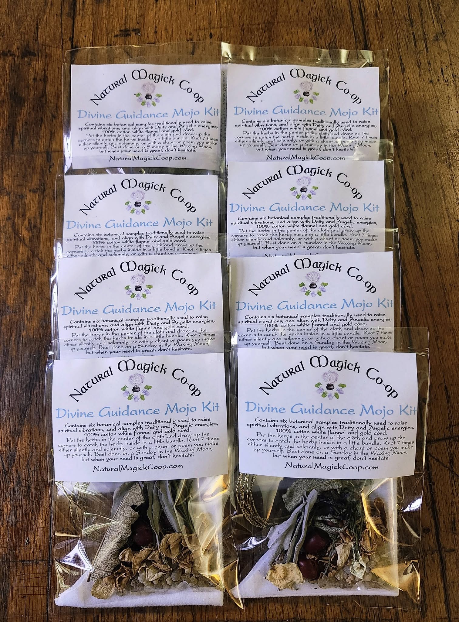 Six small packets with labels, arranged in two columns on a wooden surface, containing dried herbs or flowers.