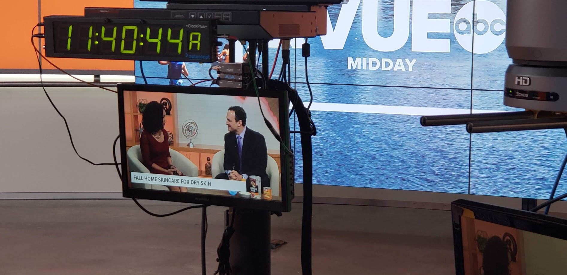 Television studio with cameras and monitors, showing a news interview, and a large screen in the background displaying 'VUE' and water.