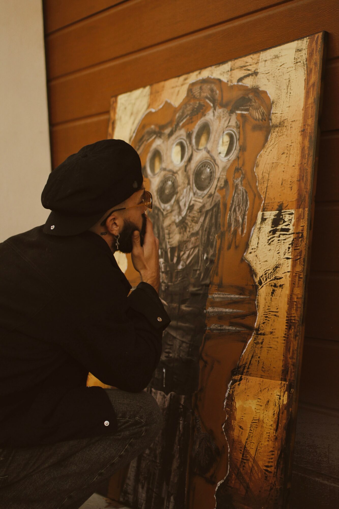 Person with a black head covering and dark clothing looks at a large abstract painting on a wooden wall.
