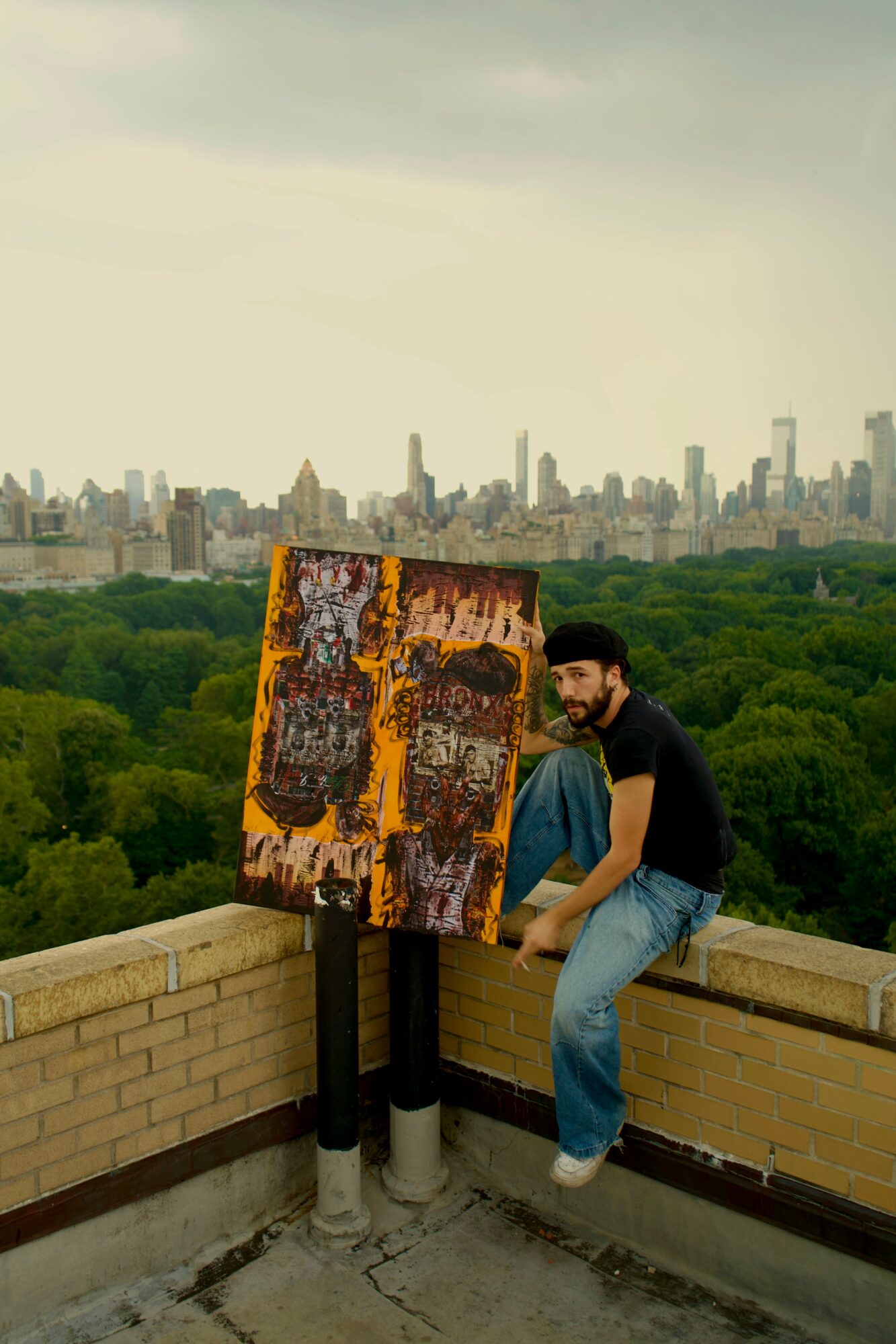 Person sitting on a rooftop ledge next to an abstract painting with a city skyline in the background.
