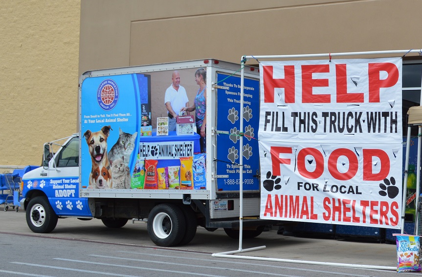 Truck with a large banner reading 'Help Fill This Truck with Food for Local Animal Shelters' parked outside.