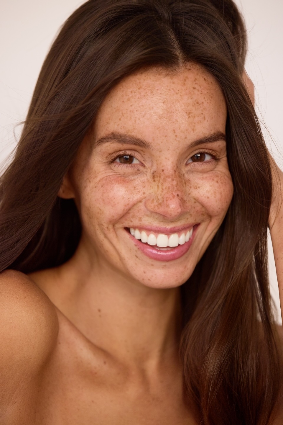 Close-up of a smiling woman with long brown hair and freckles, facing forward.