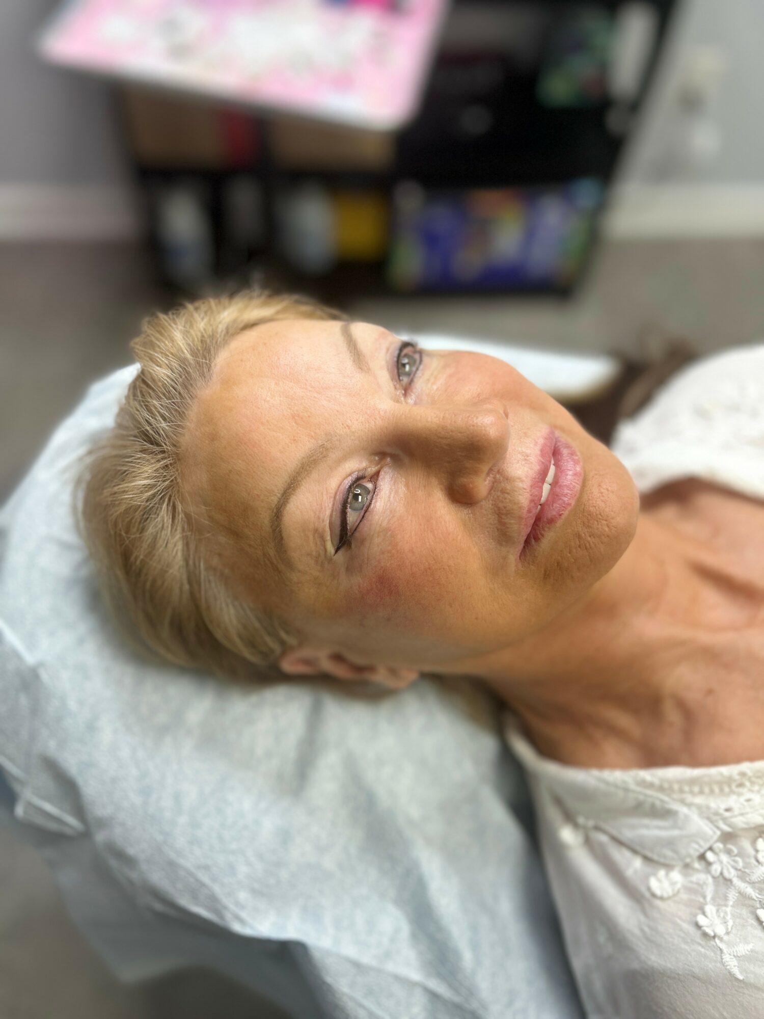 Woman lying on a medical bed with a pillow, looking upward, with a blurred background of shelves and books.