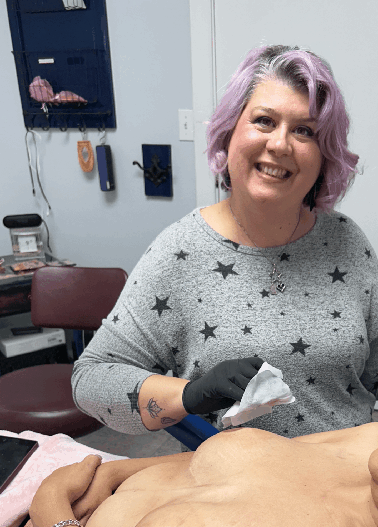 Smiling woman with purple hair wearing a star-patterned gray sweater, sitting in a medical office, holding a tissue.