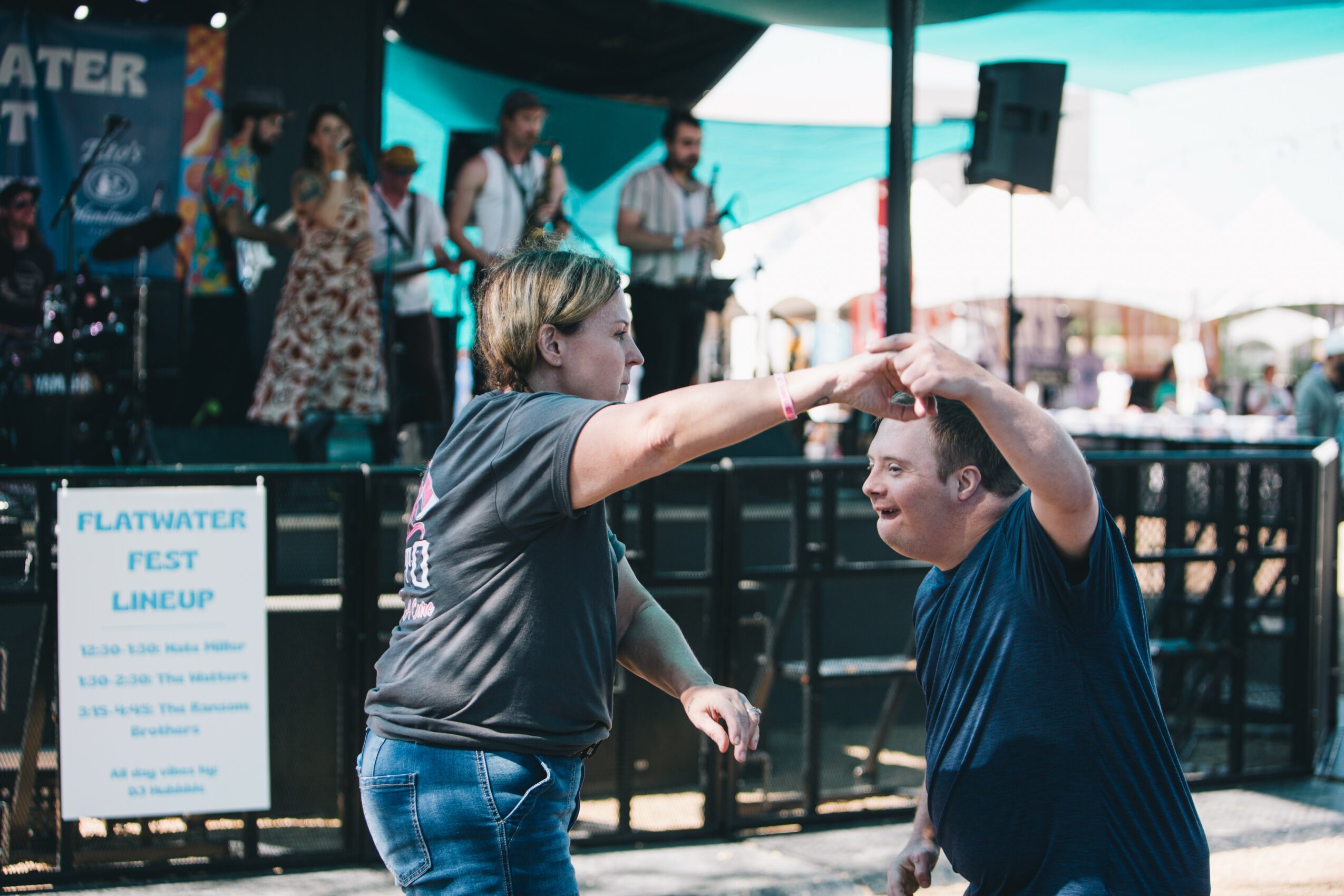 Two people dancing together at an outdoor event, with a band performing on stage in the background.