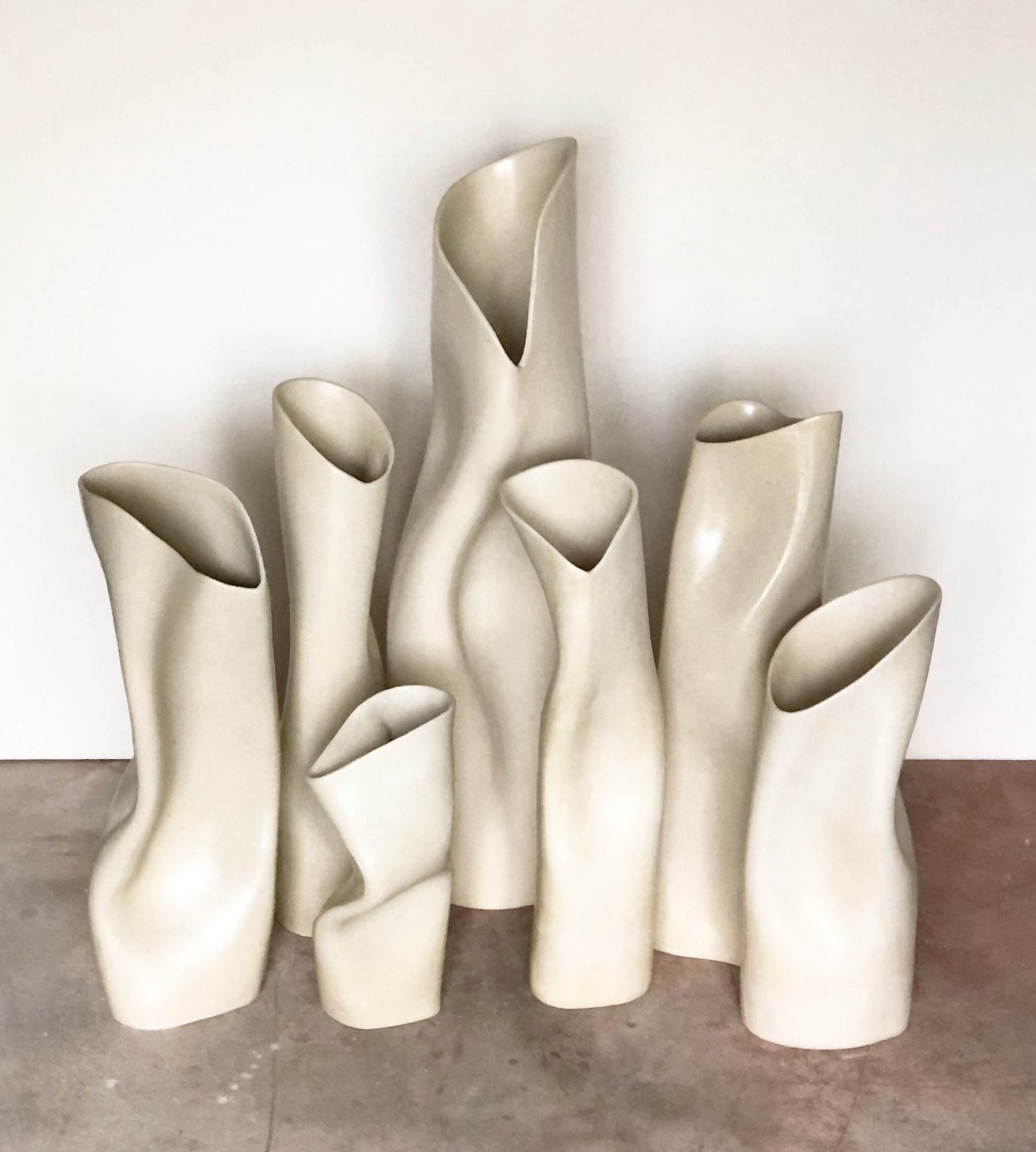 Group of tall, abstract, cream-colored sculptures with smooth, flowing shapes arranged against a white wall.