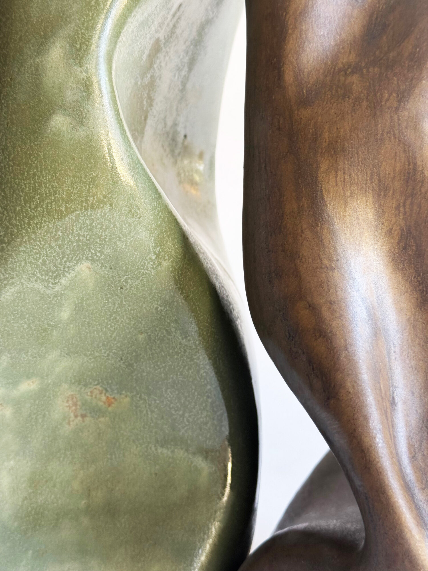 Close-up of two vases with curved shapes, one greenish and one brown, touching each other.