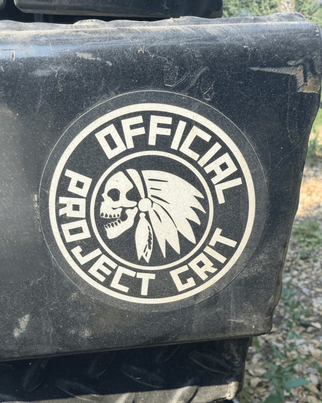 Black container with a circular logo featuring a skull wearing a feathered headdress, and the text 'OFFICIAL PROJECT GANT'.