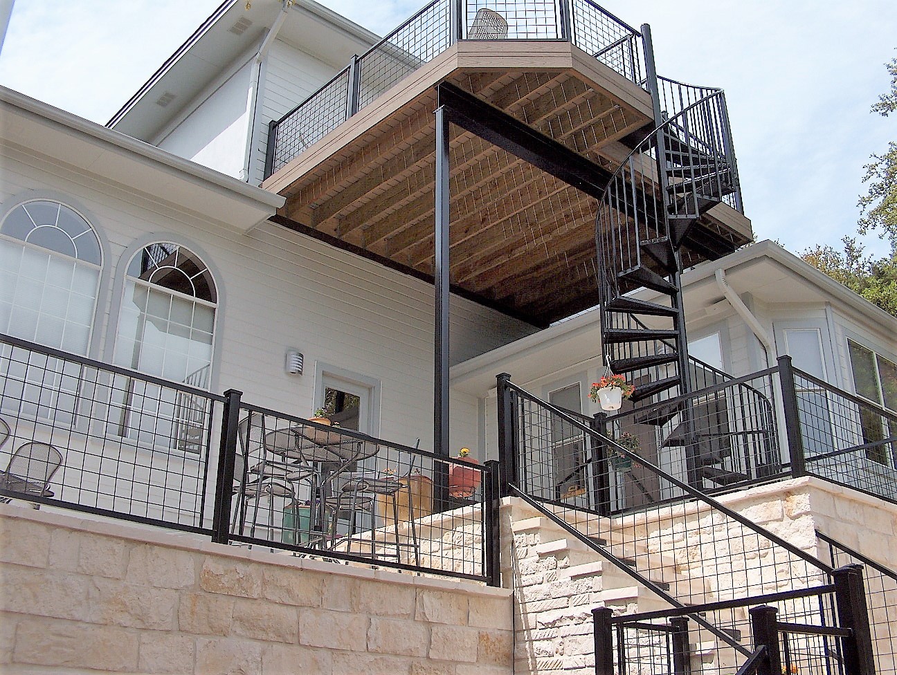 Multi-level house with balconies, stairs, and railings, viewed from below, showing different materials and architectural features.