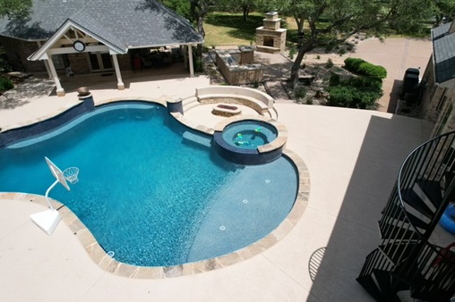Swimming pool with a hot tub and lounge chairs, surrounded by trees and a patio area.
