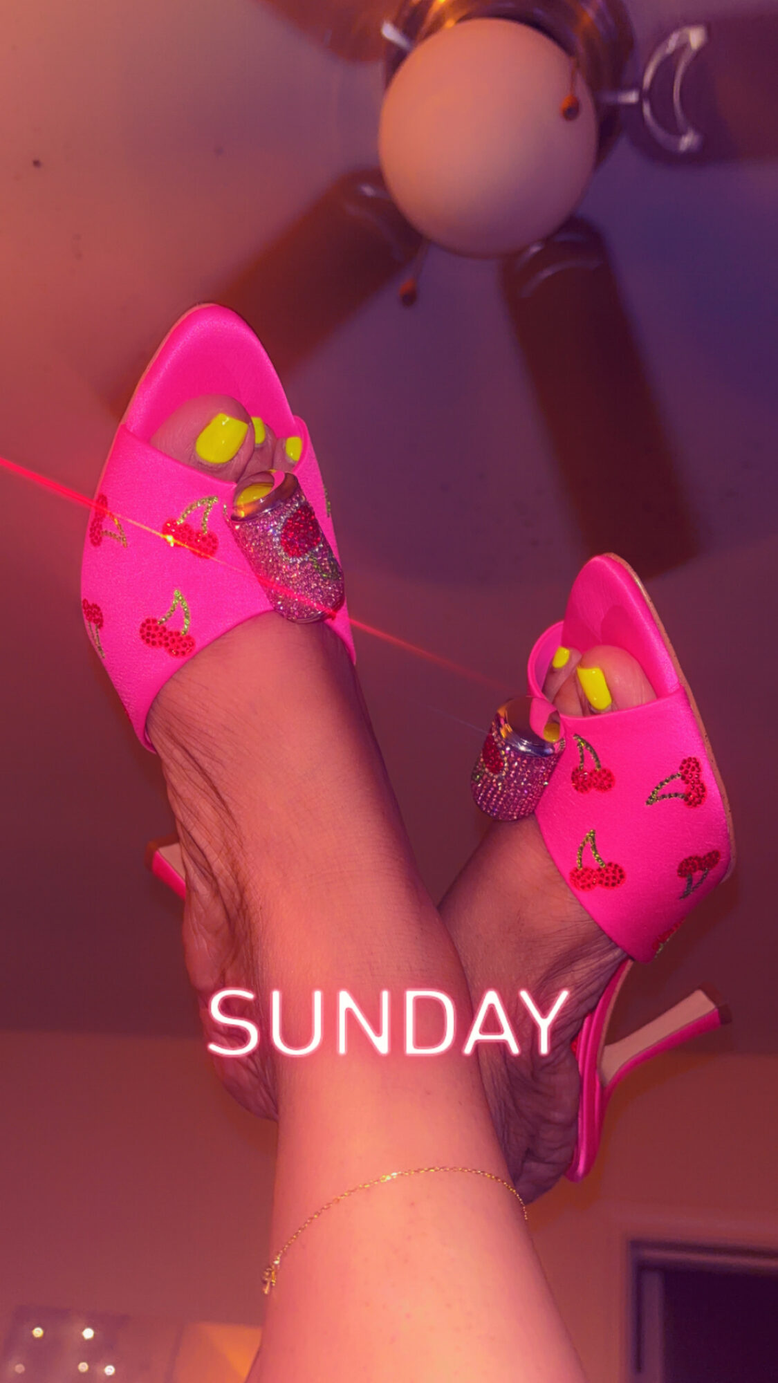 Person wearing pink high-heeled shoes with yellow bows, raised above head, ceiling fan visible, Sunday text overlay.