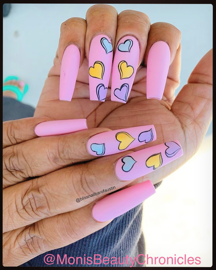 Two hands with pink and decorated nails, featuring colorful heart designs, held together against a light background.