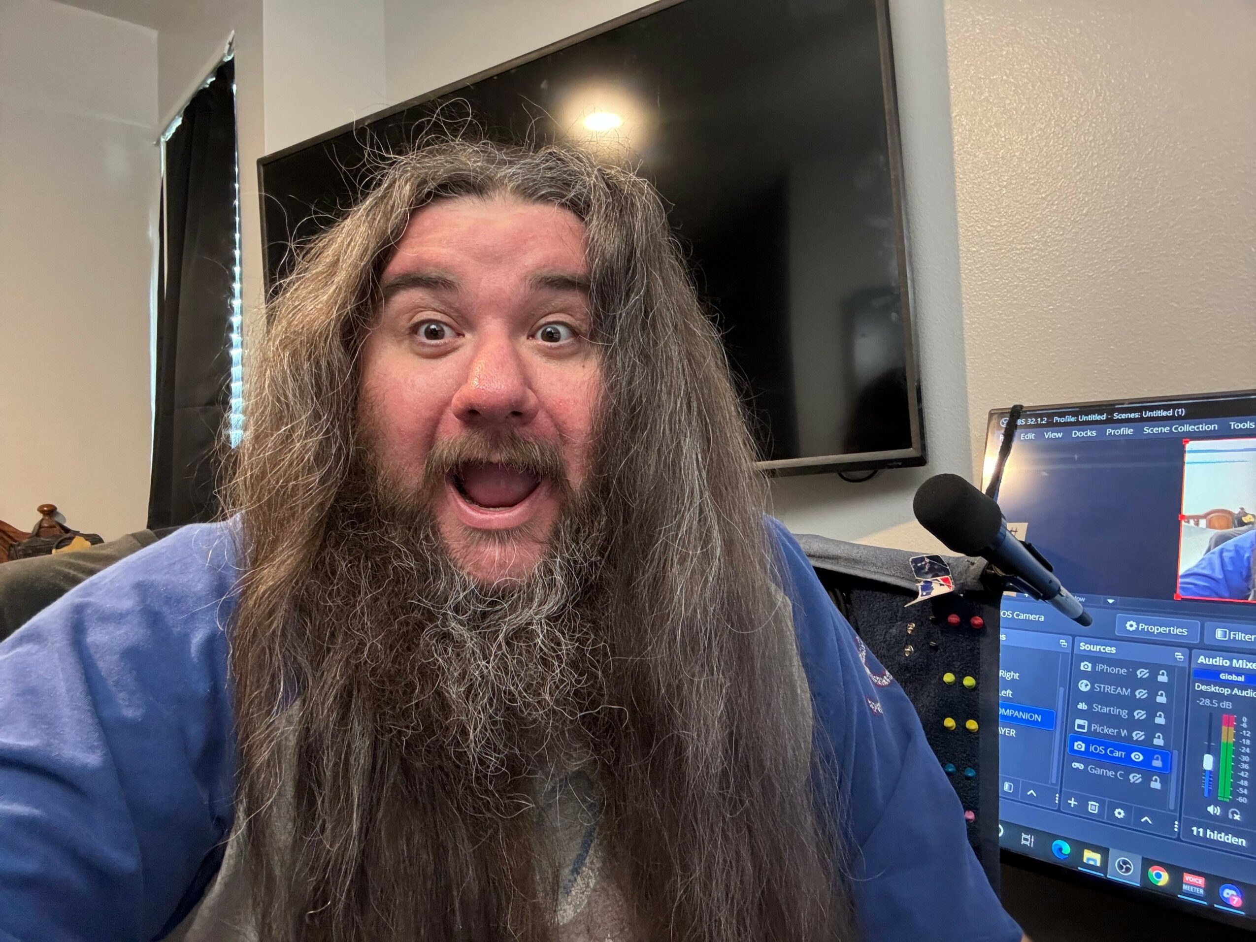 Person with long hair and beard, smiling, in front of computer monitors and a microphone.