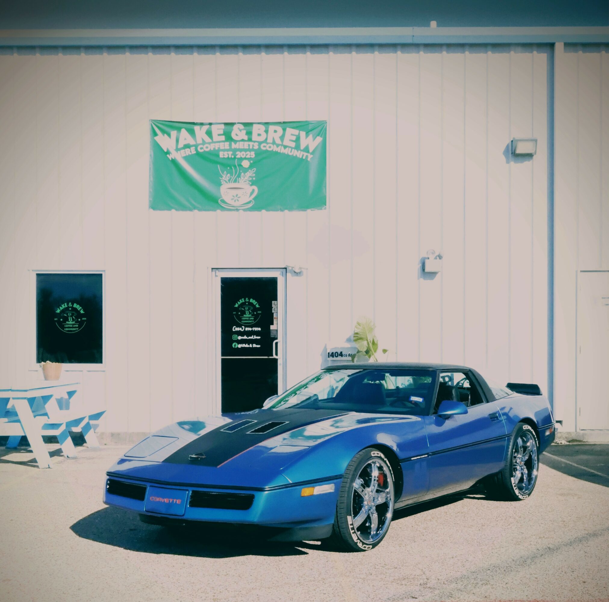 Blue sports car parked outside a building with a green sign that reads 'Wake & Brew'.