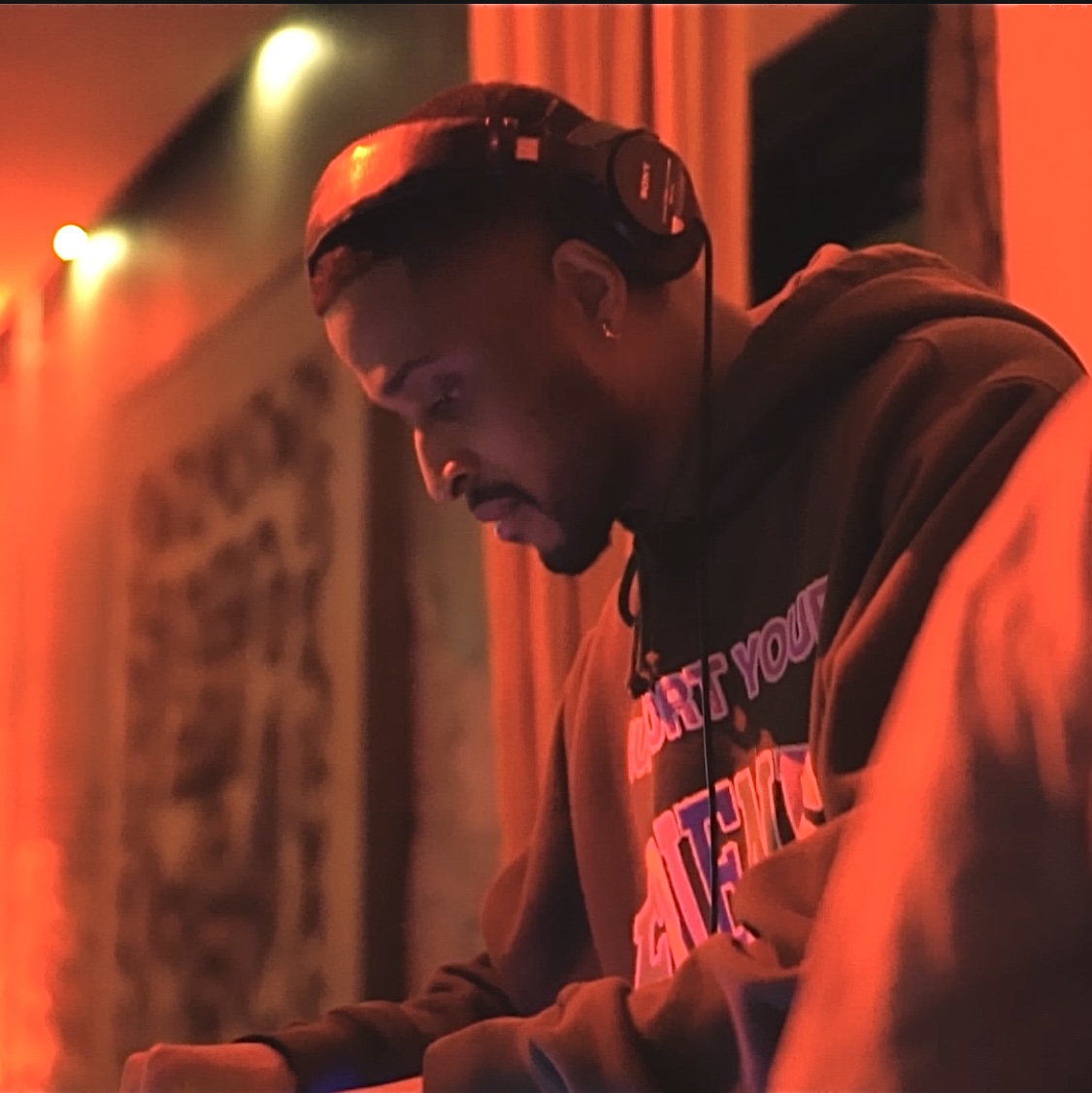 Person wearing headphones, looking down, in a dimly lit room with warm lighting and curtains.
