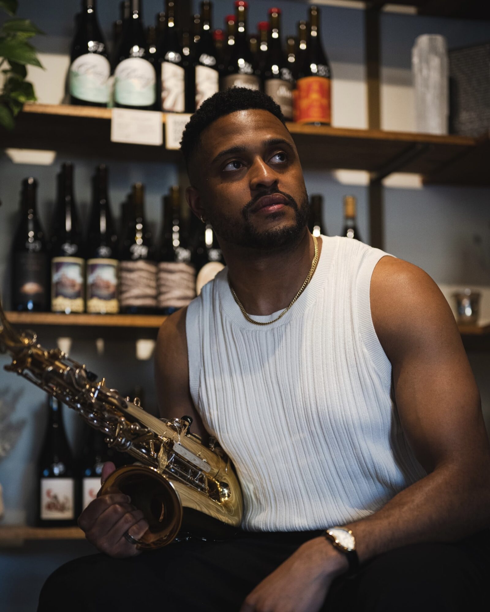 Man holding a saxophone in a bar with shelves of bottles behind him.