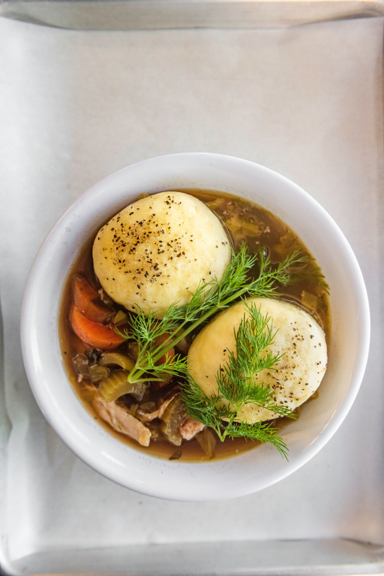 Bowl of soup with two boiled eggs, herbs, and vegetables, served in a white bowl on a tray.