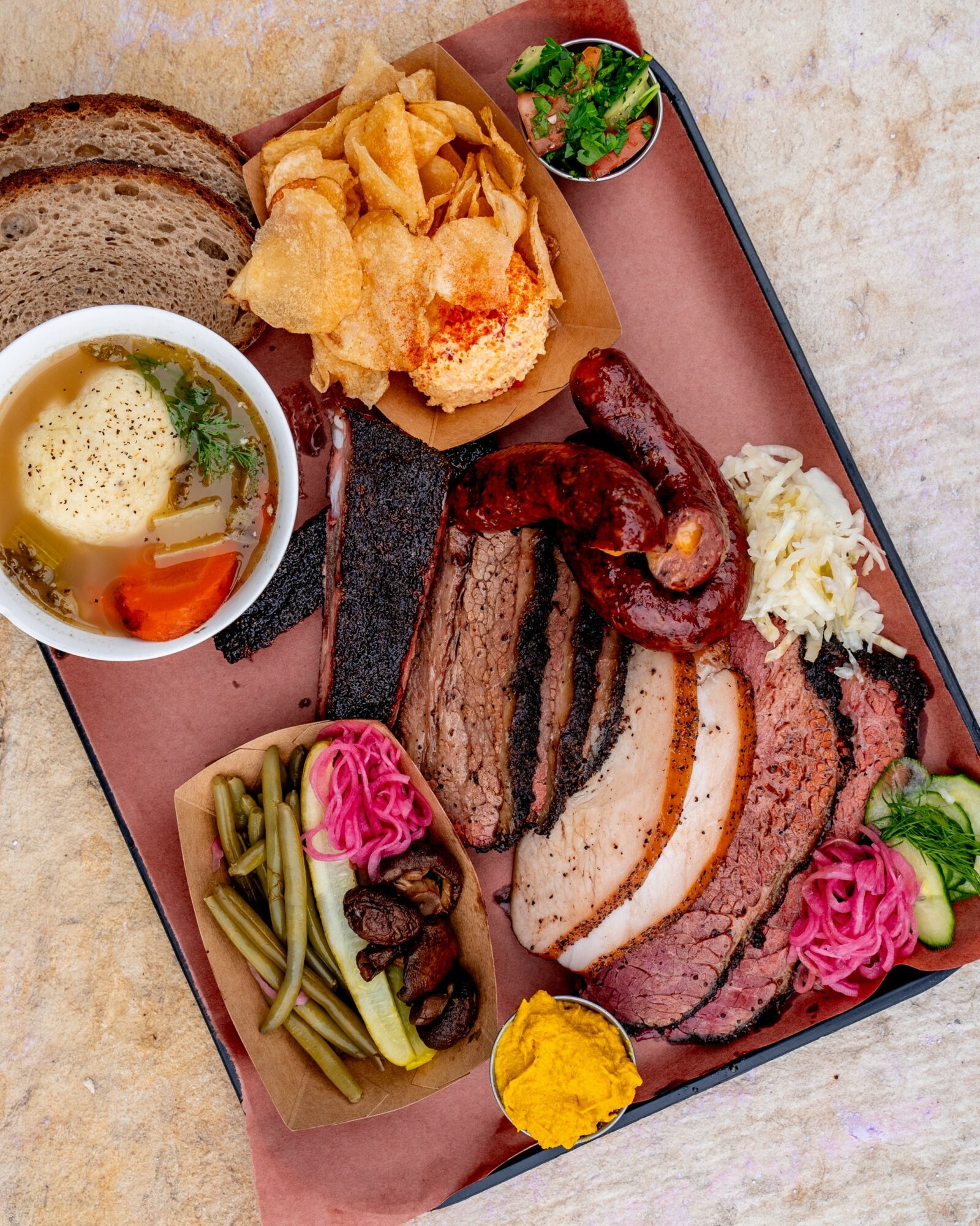 Assorted grilled meats, vegetables, and side dishes on a tray, including steak, sausage, fried items, and pickled vegetables.