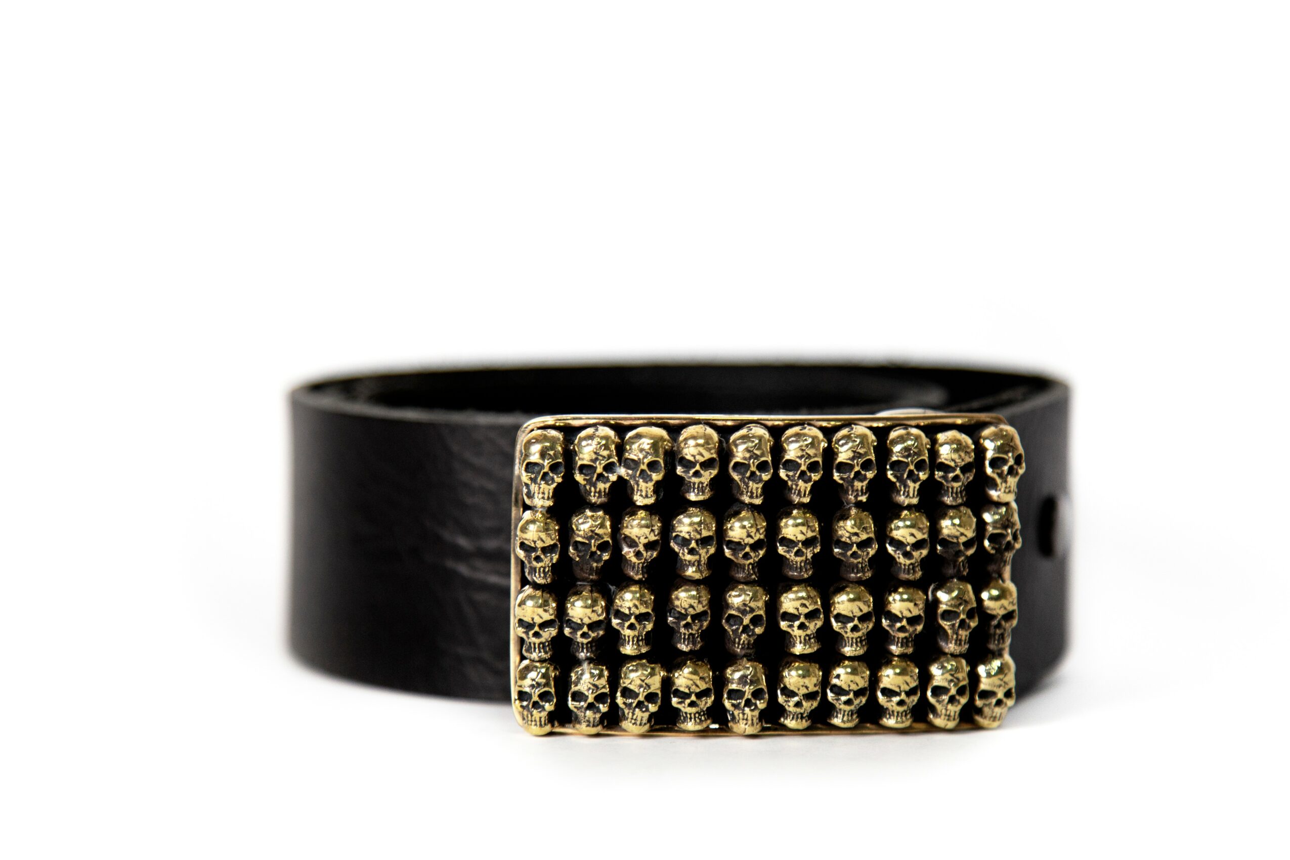 Black belt with a rectangular gold-colored buckle decorated with multiple small skulls, against a white background.