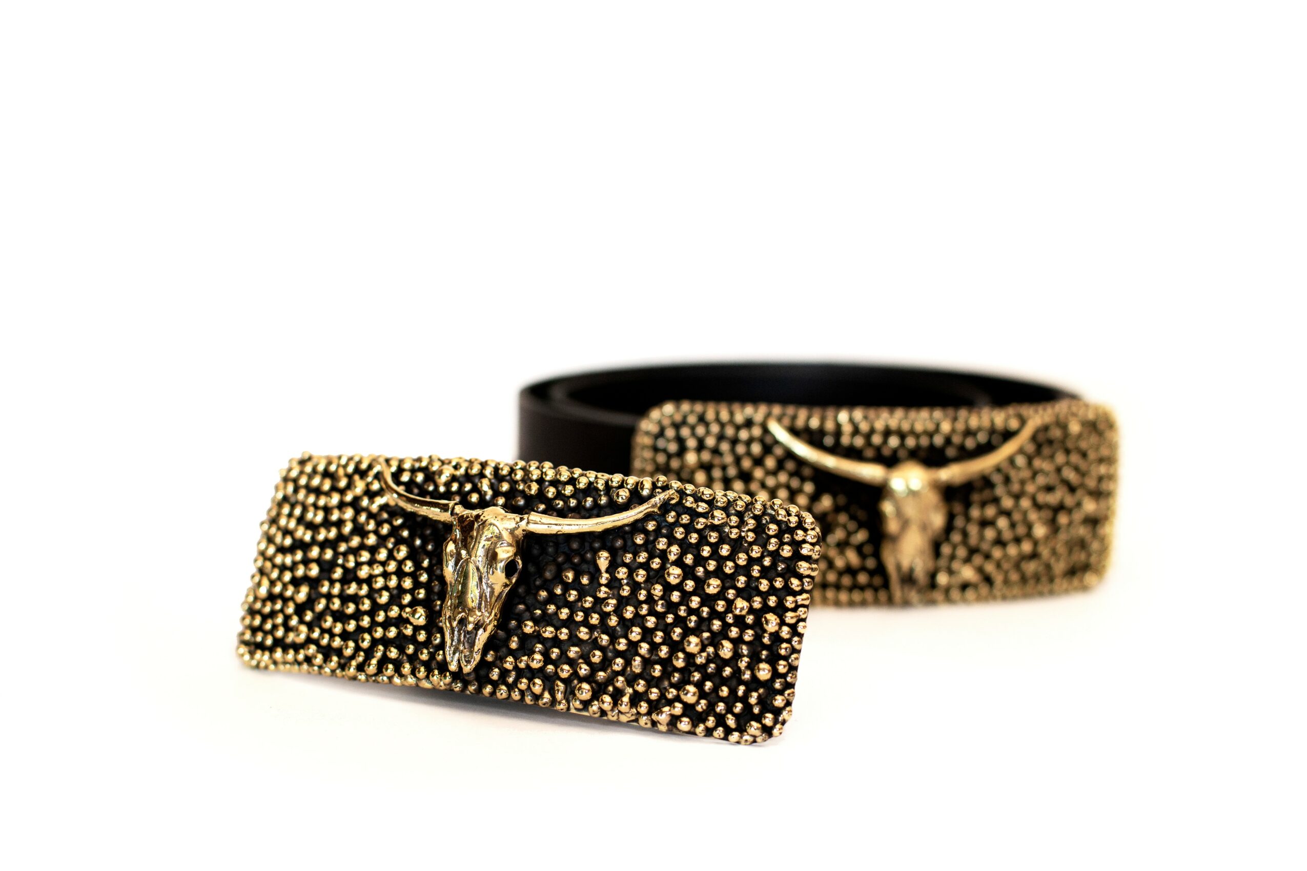 Two black belts with gold-studded buckles, one rolled and one flat, on a white background.
