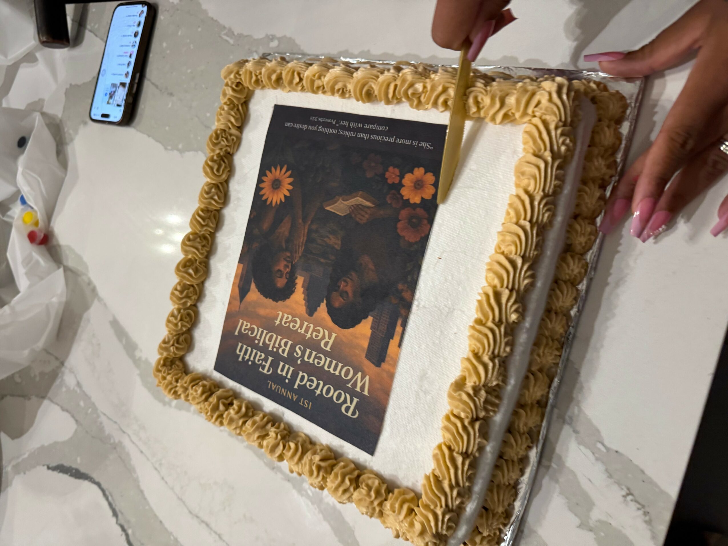 Person cutting a rectangular cake with a printed edible image on top, decorated with yellow frosting border, on a white table.