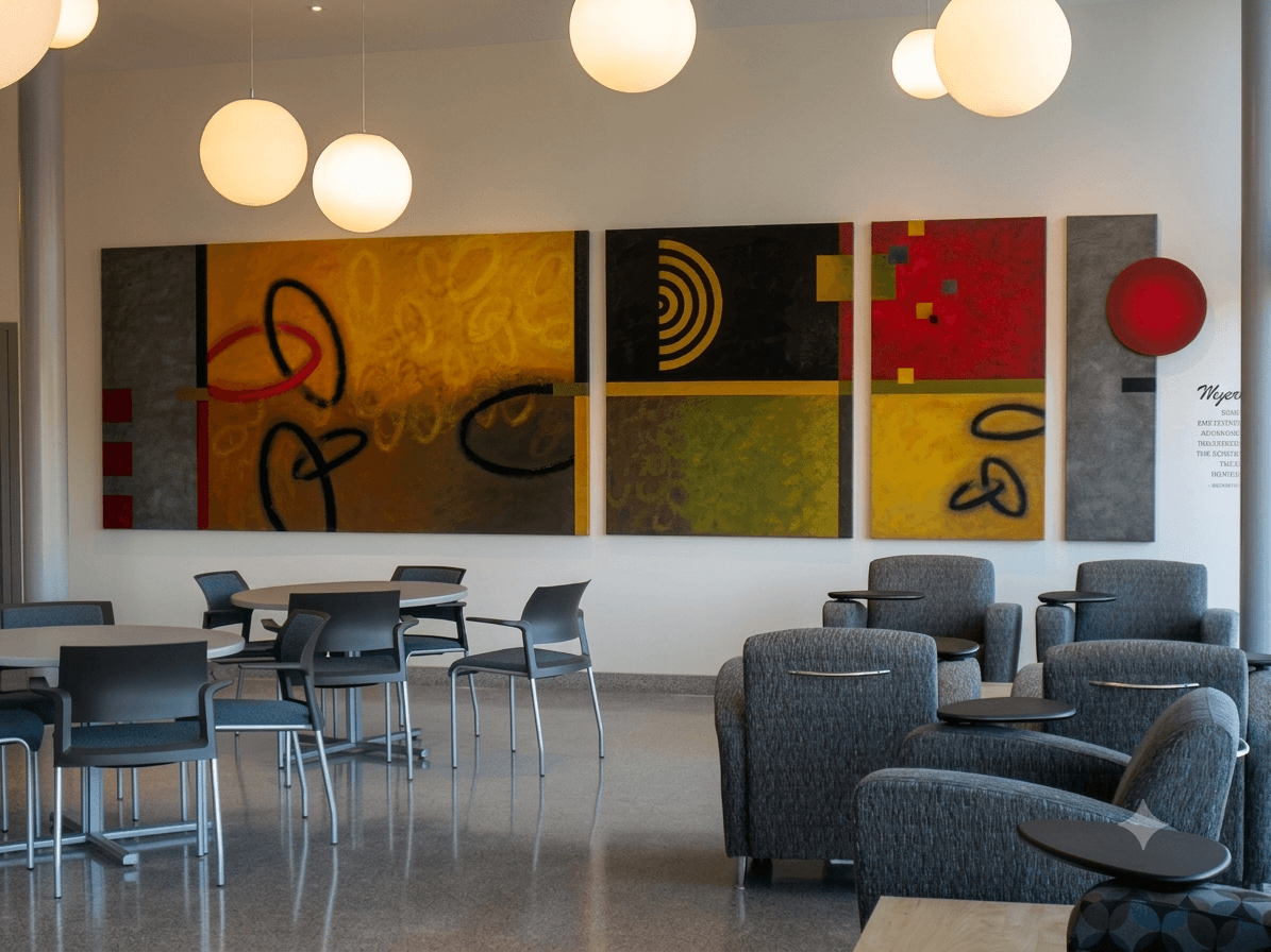 Modern lounge with abstract artwork on the wall, round hanging lights, tables, and chairs, and a seating area with armchairs.